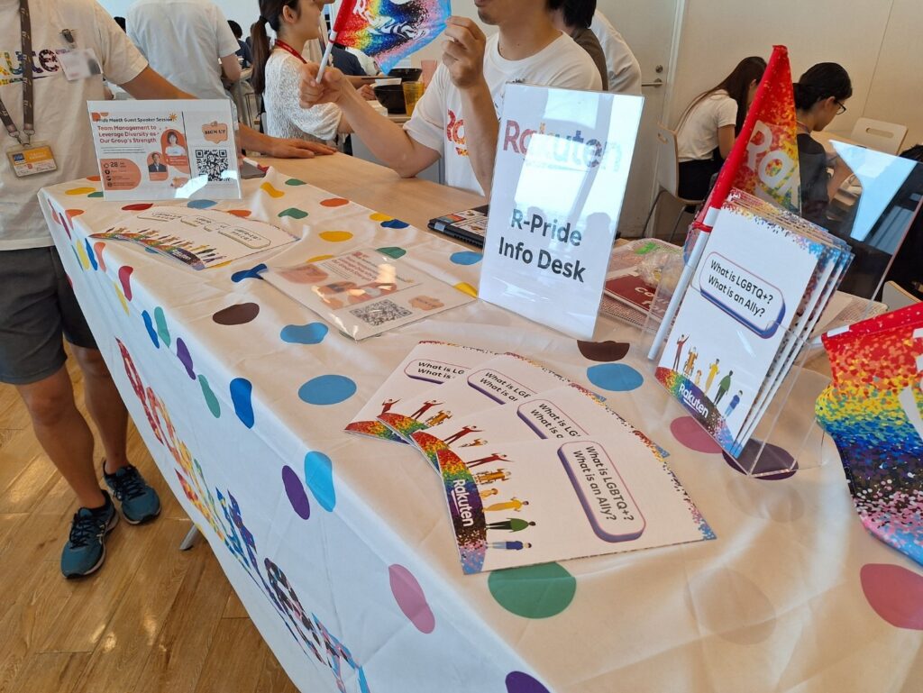 本社カフェテリアにしてインフォメーションデスクを開催。レインボーテーブルクロスをかけ、アライ冊子を配布している。